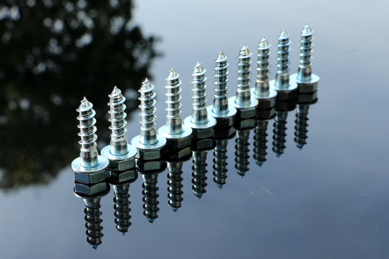 A row of shiny metal screws on a reflective surface with clear reflections.